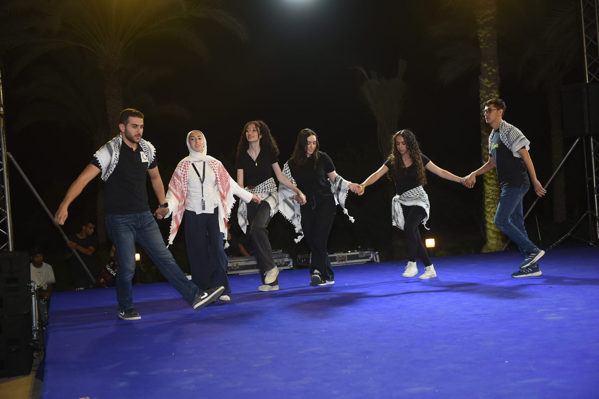 Scholars performing a dabke on stage in traditional keffiyehs