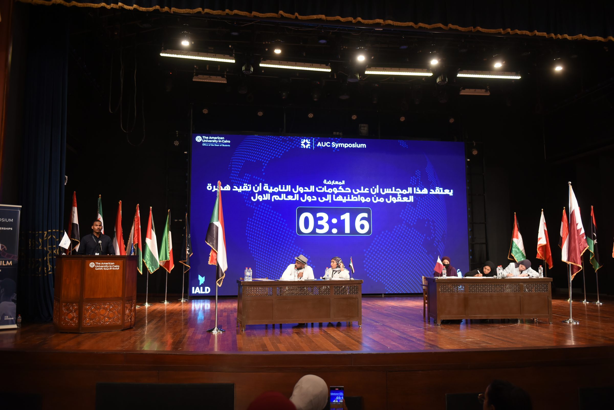 The debate stage with the motion displayed and the flags of the region