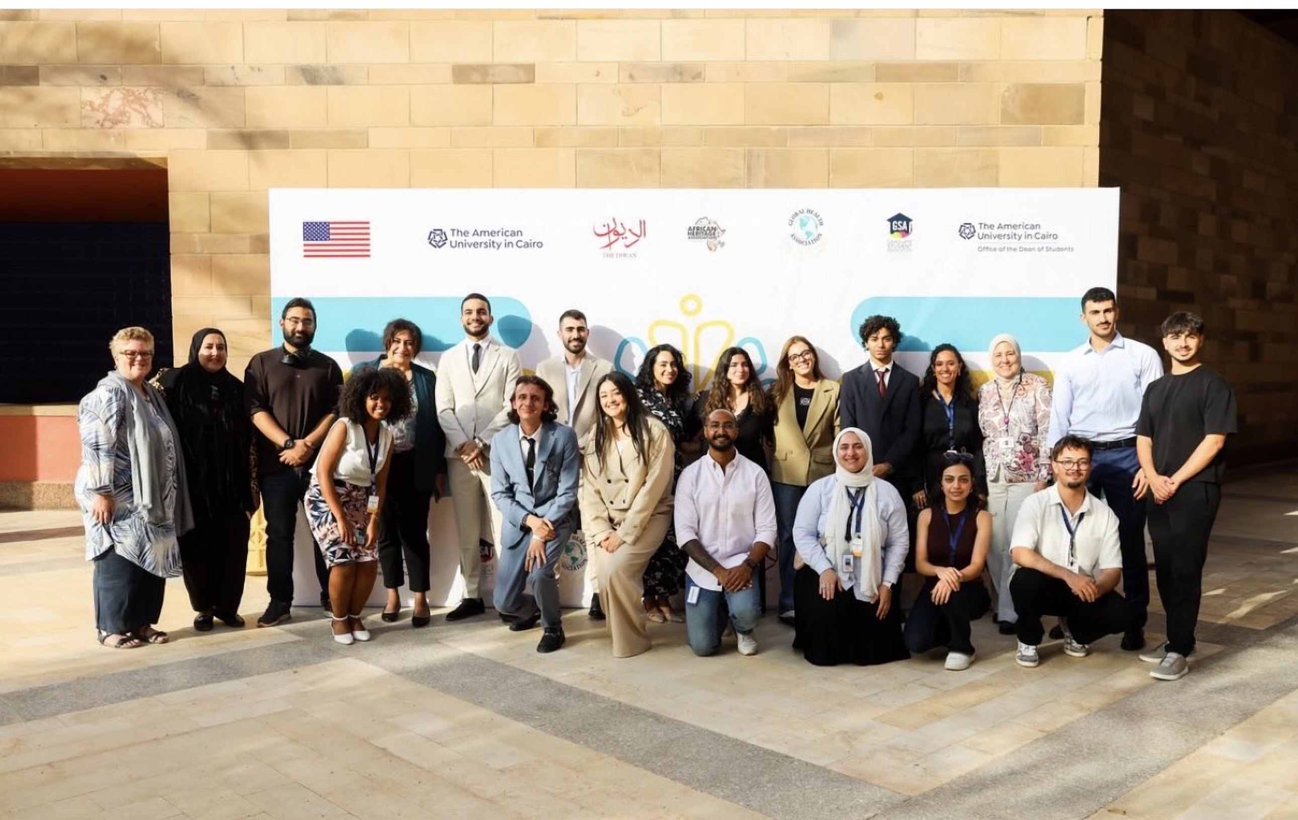 Participants and staff photographed outdoors in front of the symposium banner