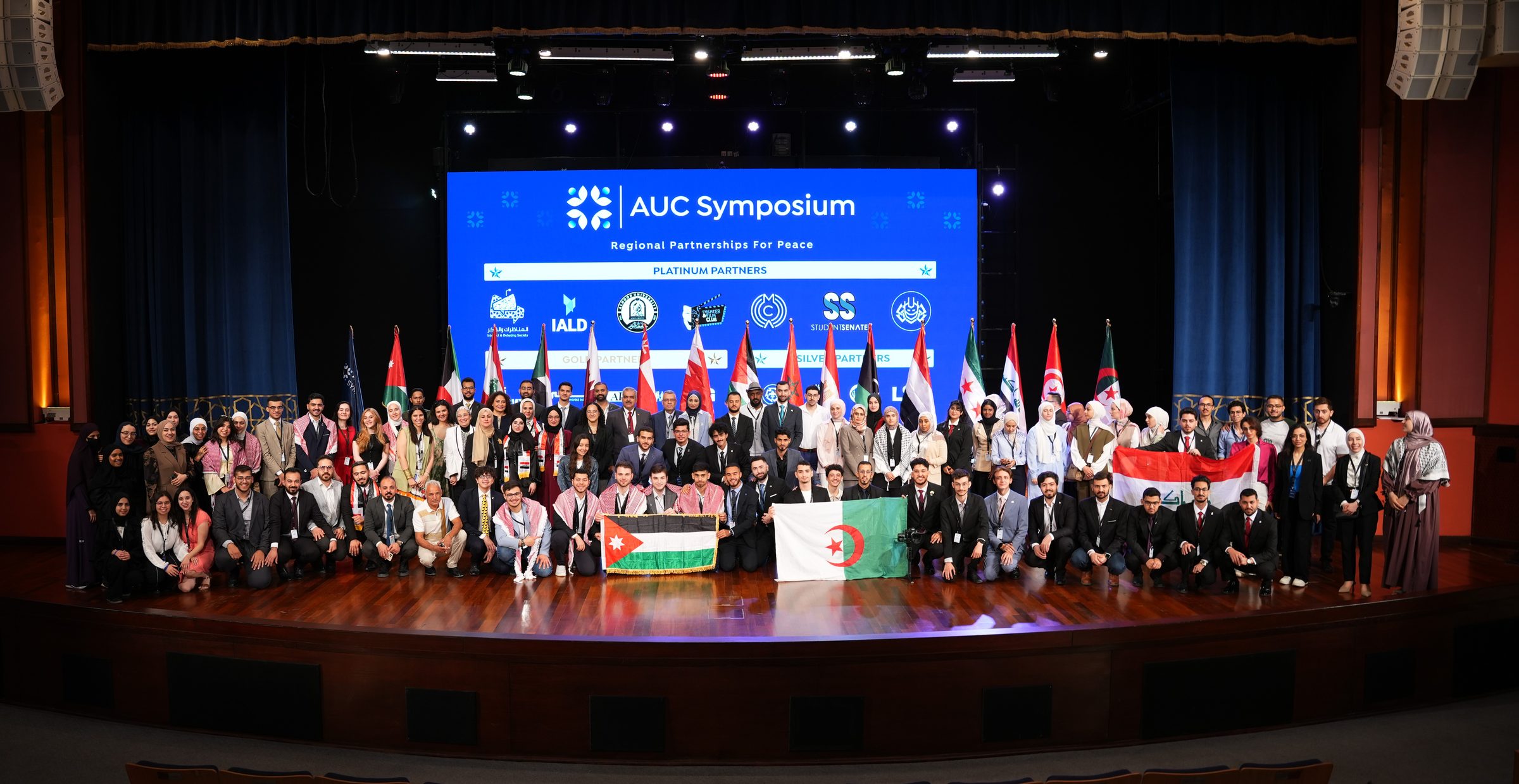 Participants of the AUC Symposium gathered on stage with the flags of the region